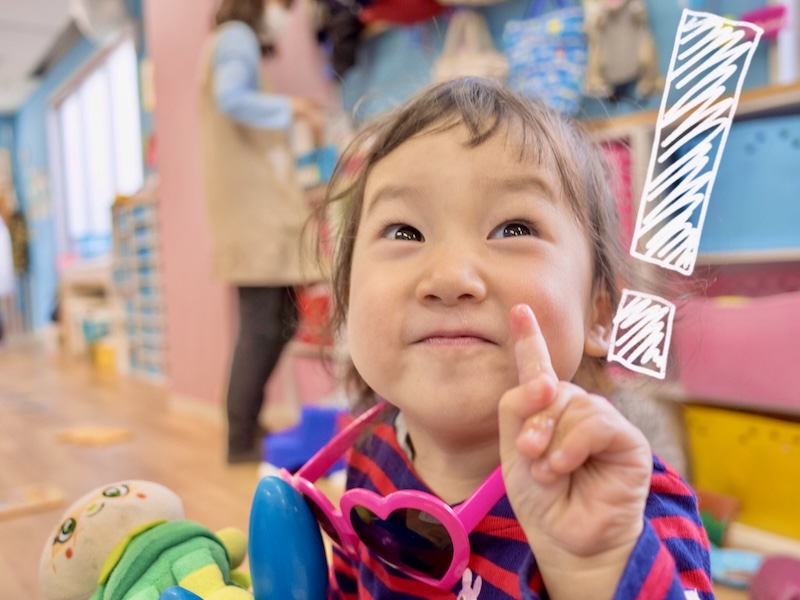 清潔感のある広々としたkidsroomにじいろの保育室。手前ではお友だちが座って遊んでいる、穏やかな日常風景。