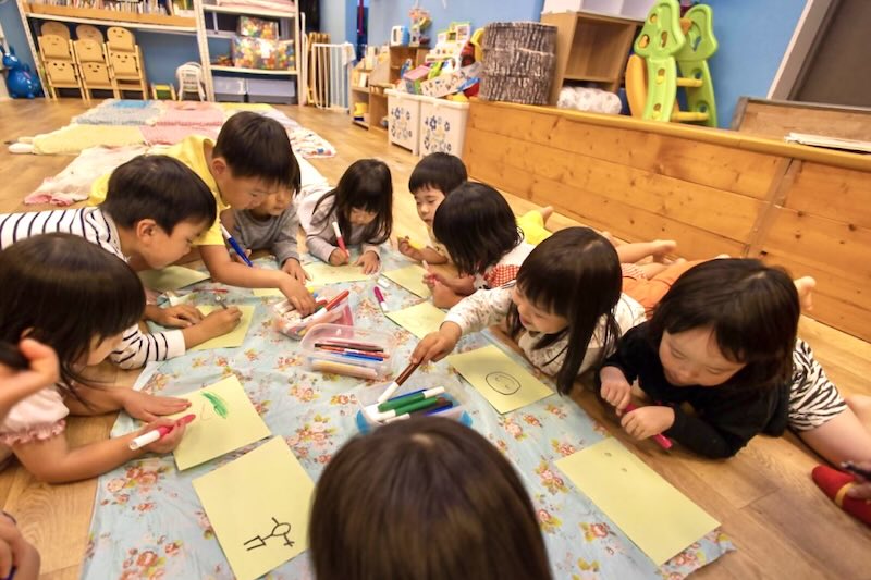 静岡市の「kidsroomにじいろ」で、お友だちと一緒にみんなでお絵描きを楽しむ様子。 大きな紙を囲んでクレヨンで自由に描いている。