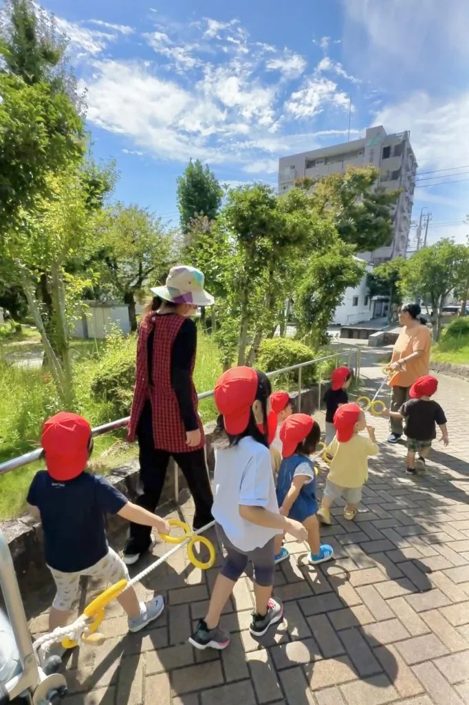 お散歩ロープを持って常磐公園を元気に歩く園児と保育士の様子